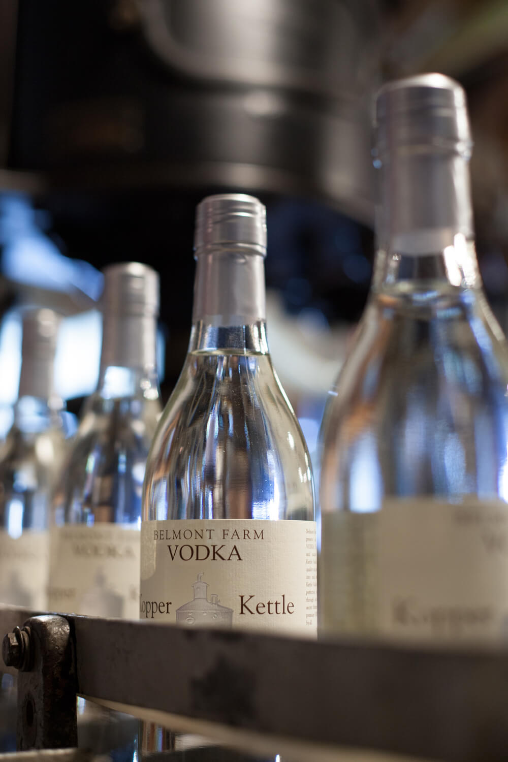 Close-up of multiple Belmont Farm Vodka bottles in a row. The bottles are clear with silver caps, and the label reads 