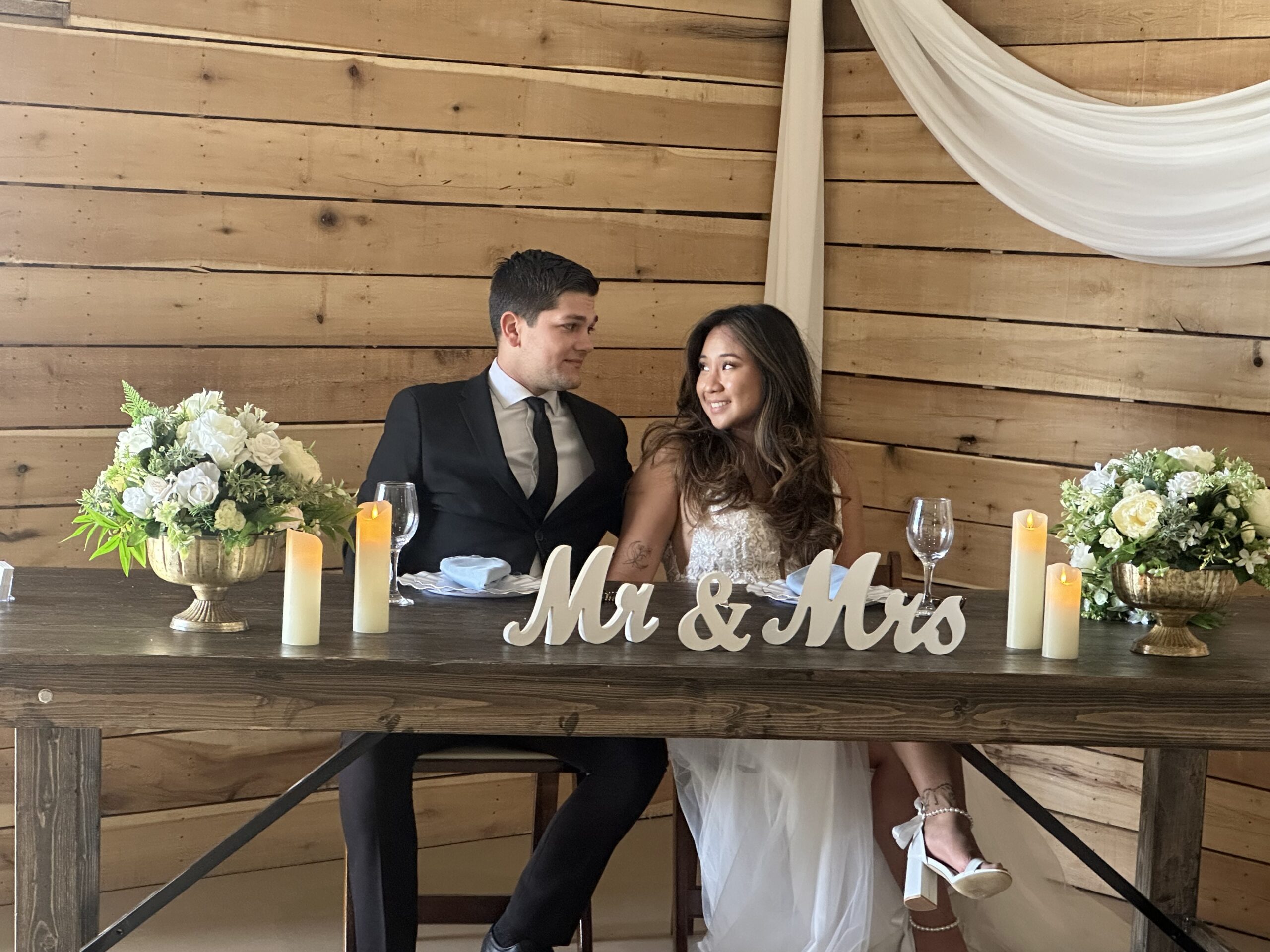 A newlywed couple sits at a rustic wooden table with