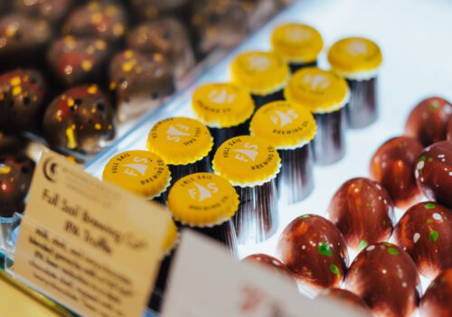 A display case filled with assorted chocolates, including brown chocolates with specks, yellow-wrapped chocolates with the letter 