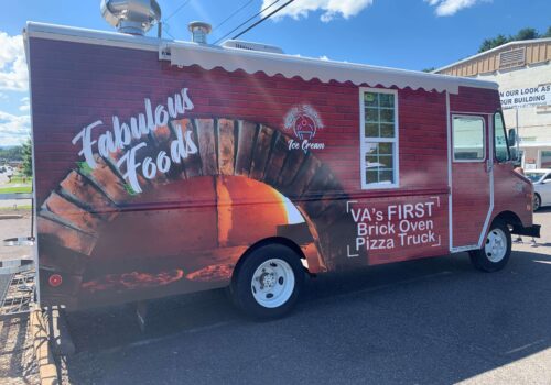 A food truck with a red brick oven design on its side is parked. The text on the truck reads 
