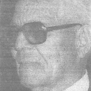 A grayscale image of an older man with short hair wearing dark sunglasses and a suit. The picture is slightly grainy, giving it a vintage appearance.
