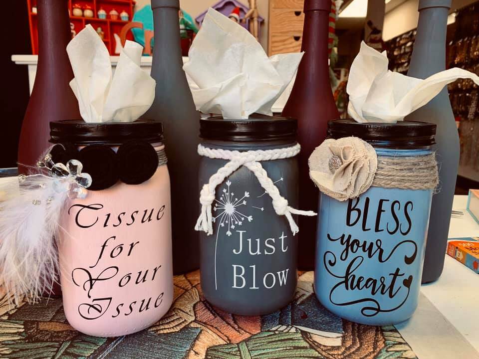 Four decorated tissue holders made from jars are displayed. The jars are painted in pastel colors with phrases such as 