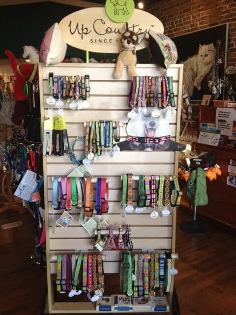 A display rack in a pet store showcasing a variety of colorful dog collars. The shelves are filled with neatly arranged collars in different patterns and sizes. The top of the rack has a sign labeled 