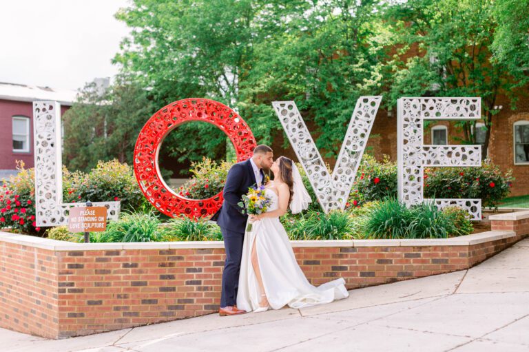 A bride and groom kiss in front of a large, decorative 
