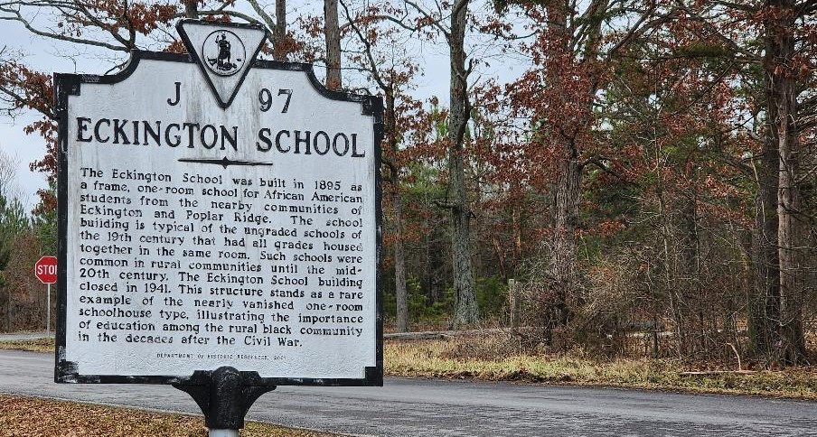 A historical marker for Eckington School, a one-room school built in 1905 for African American students, stands on a rural roadside. Bare trees line the background. The sign highlights the school's significance and its closure in 1941.