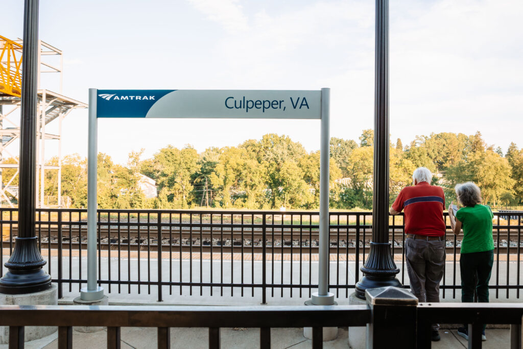 two people standing at an Amtrak platform with a sign that reads Culpeper