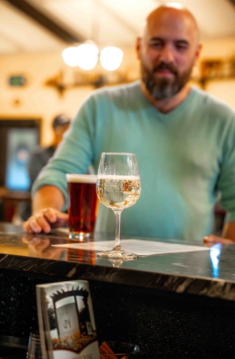 man standing at a bar with a beer and glass of wine