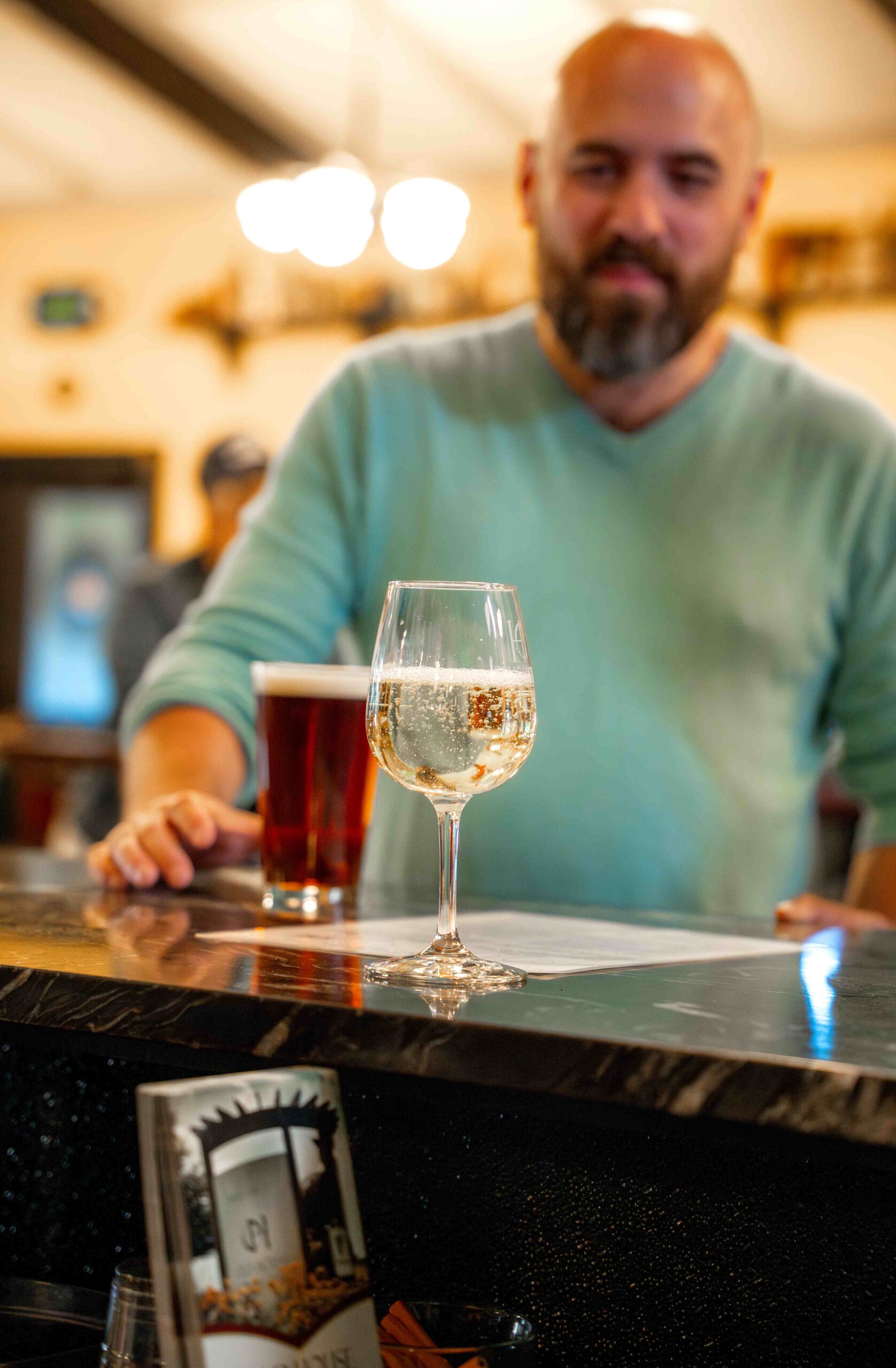 man standing at a bar with a beer and glass of wine