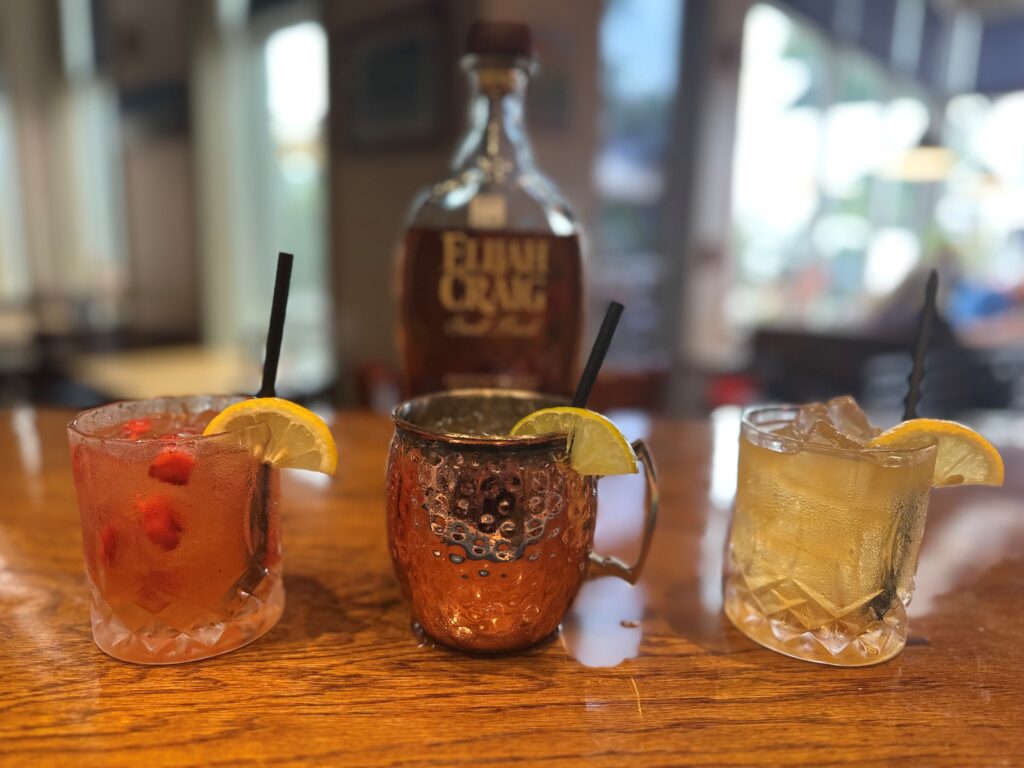 three mixed drinks with a bottle of Elijah Craig in the background