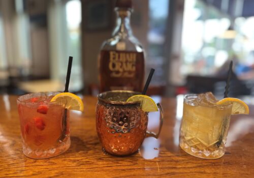 three mixed drinks with a bottle of Elijah Craig in the background Image